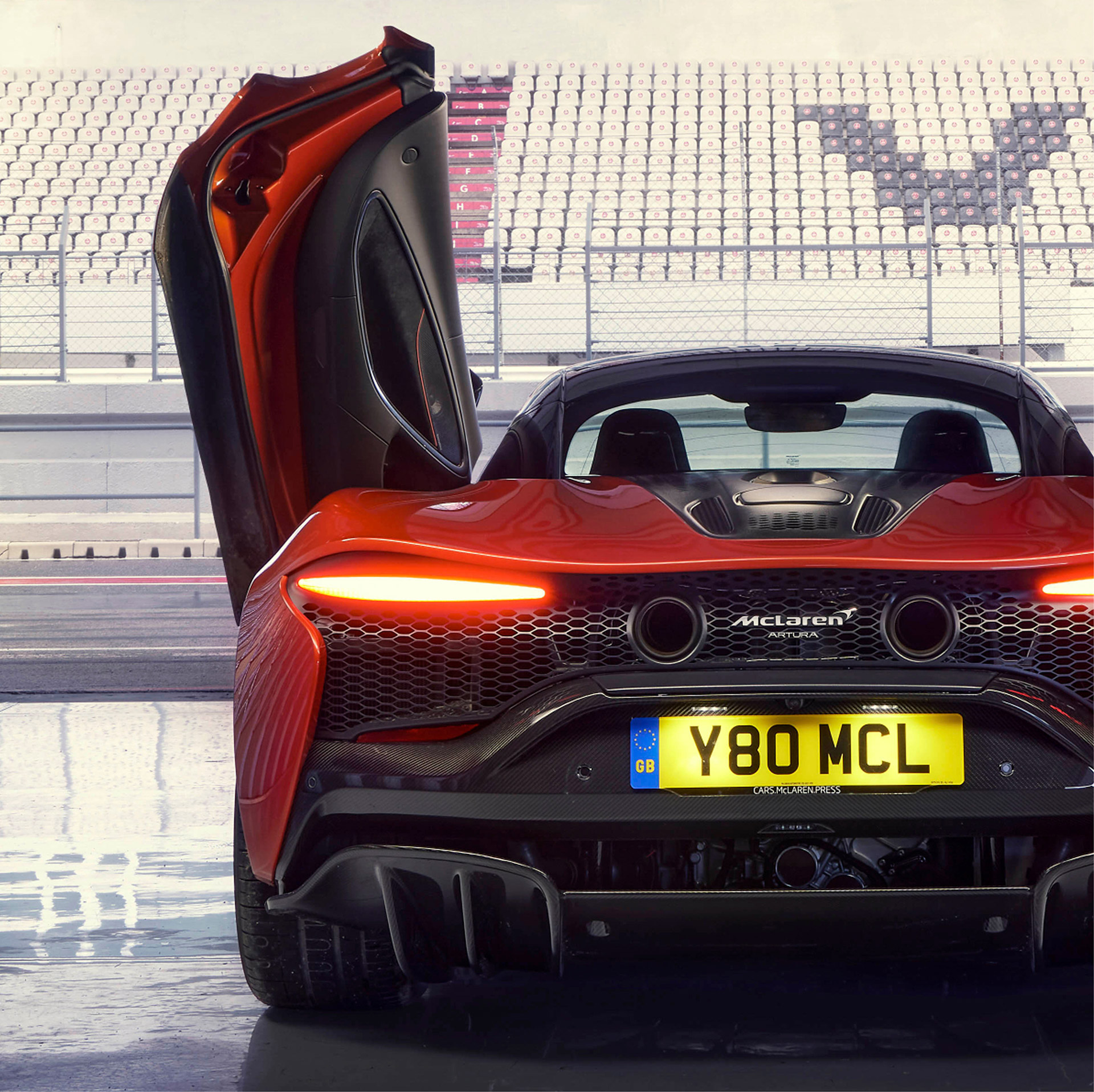 Red McLaren Artura rear with open passenger side door.