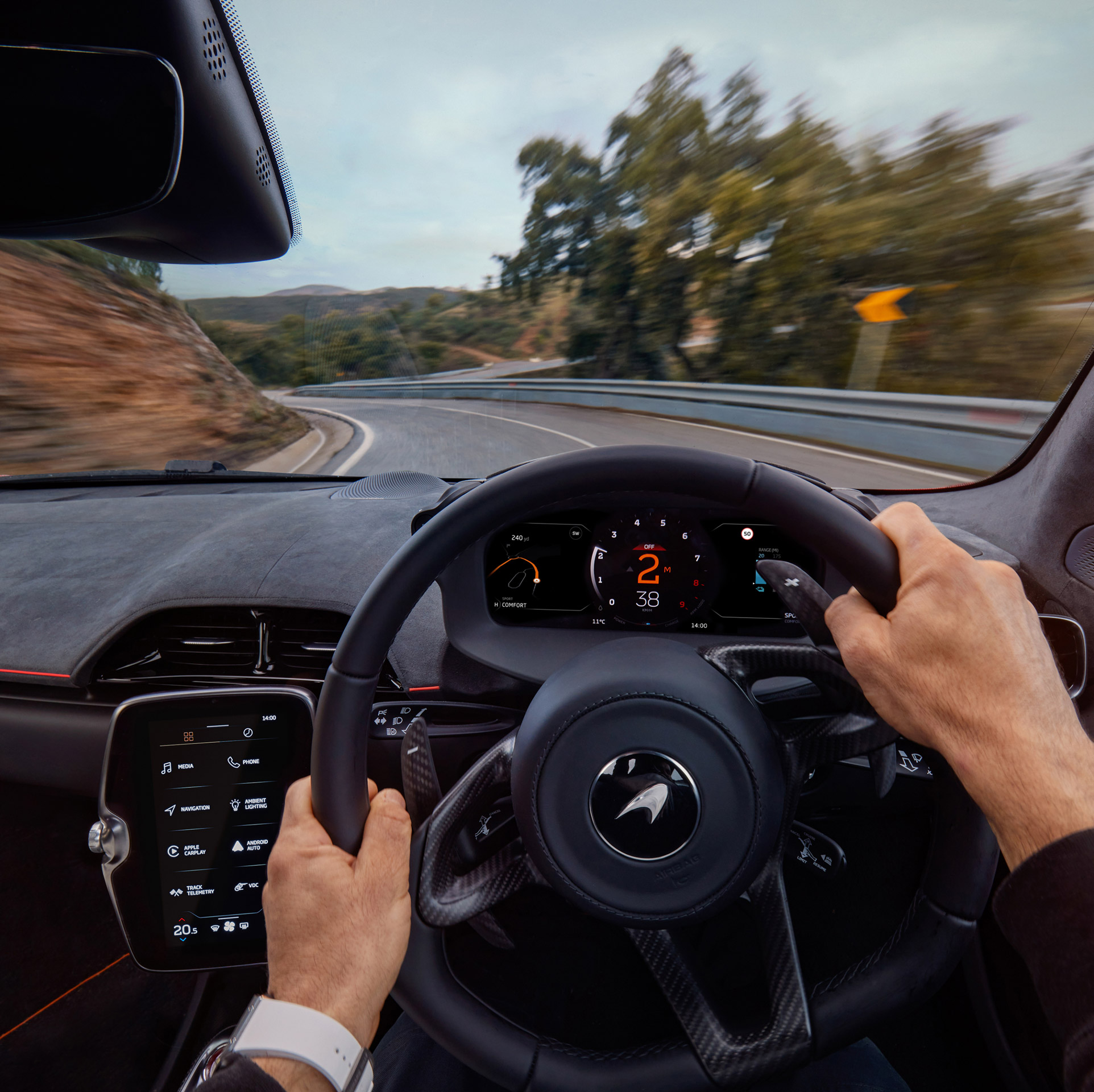 Hands holding a McLaren Artura steering wheel while driving at speed.
