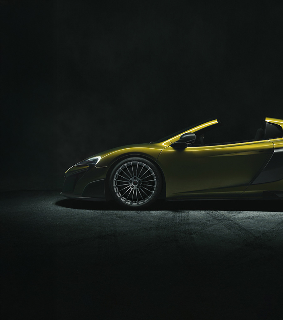 Side view of olive green McLaren 675LT Spider, photographed in a dark studio environment.