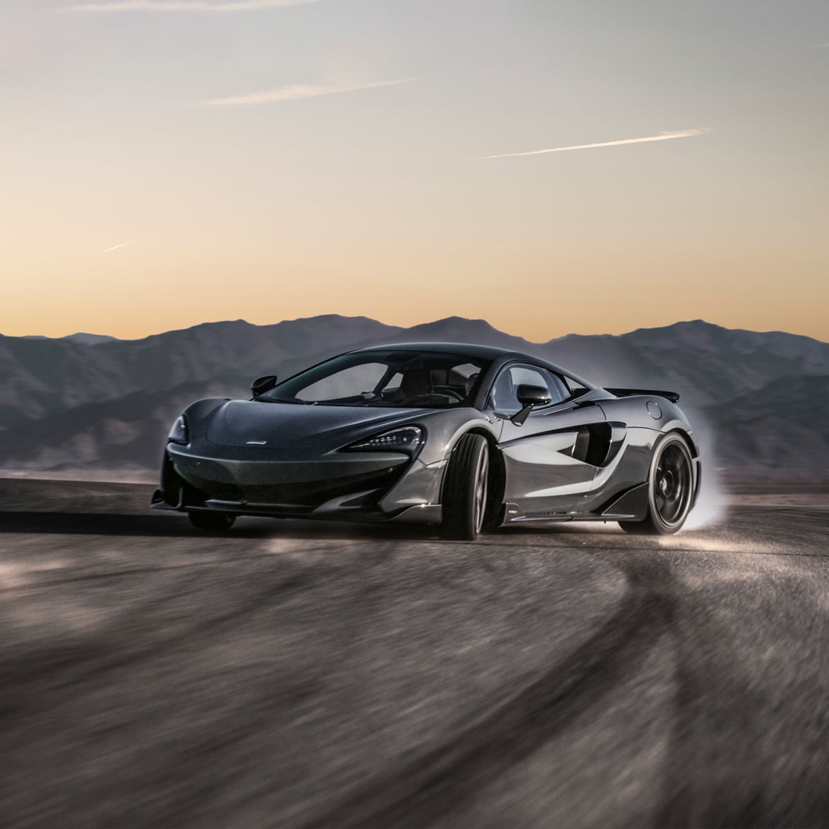 McLaren 600LT driving in a bend on tarmac at high speed. Blurry mountains can be seen in the background.