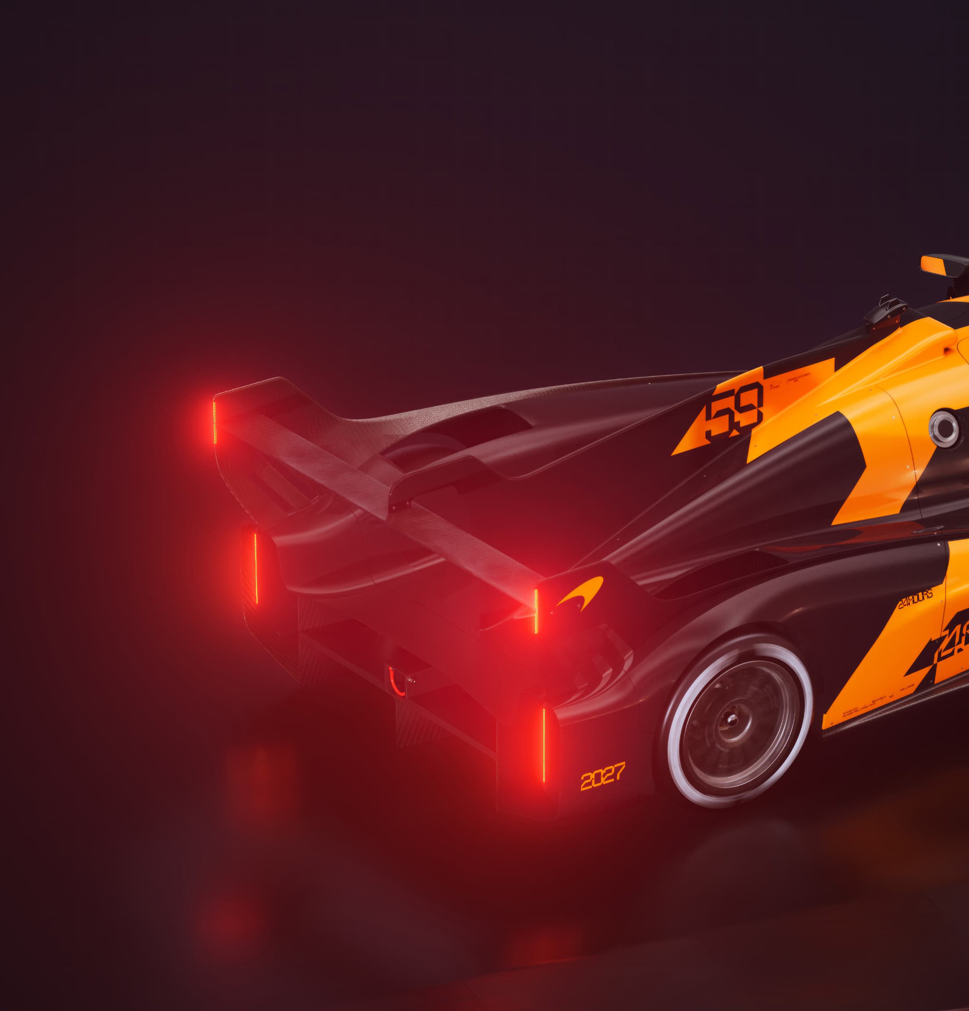 A rear-three-quarter view of a black and orange McLaren endurance race car prototype, showcasing its glowing red brake lights and intricate aerodynamics in a dark setting.