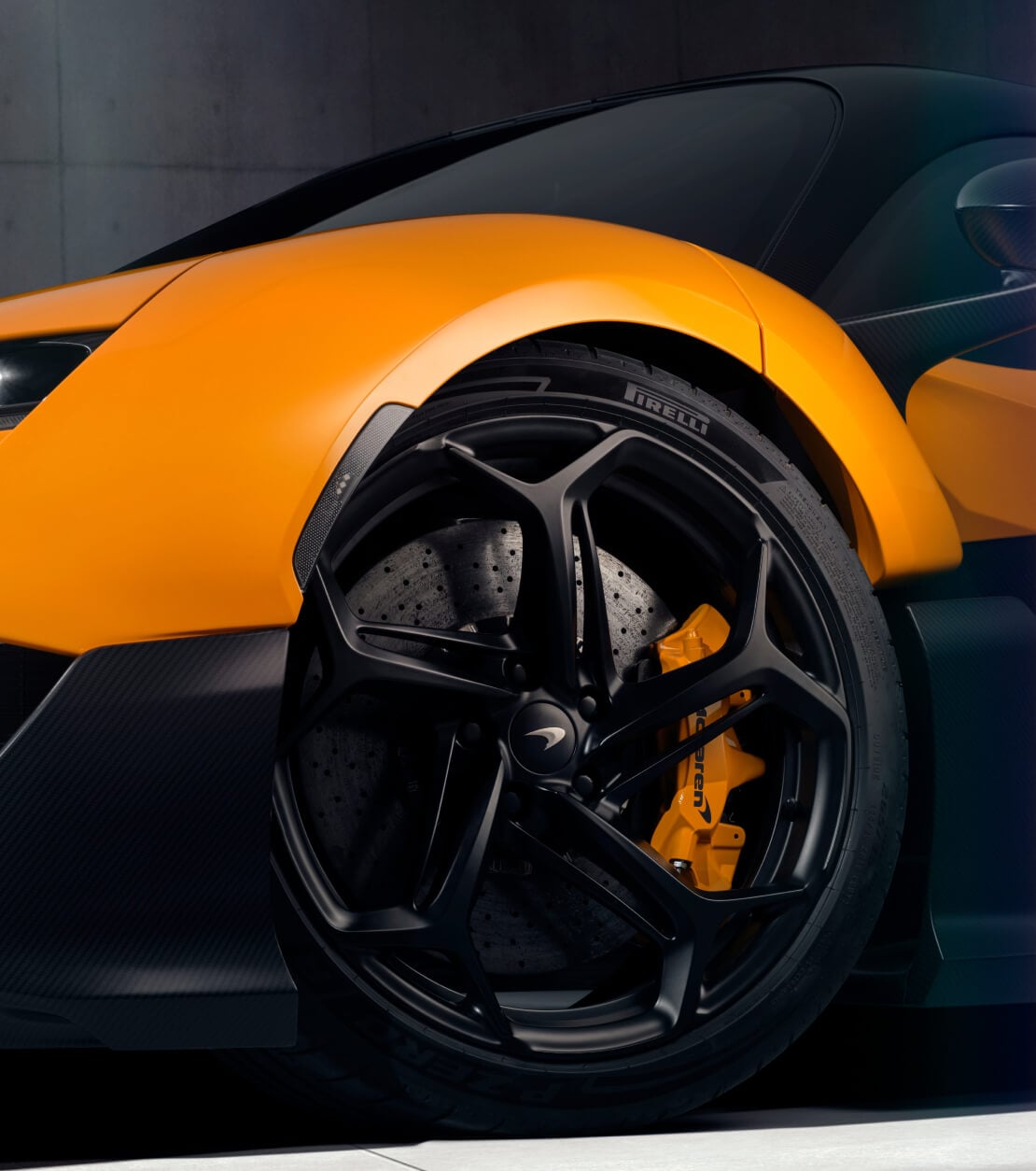 A close up of a black wheel that is slightly turned with an orange brake calliper on an orange McLaren W1.