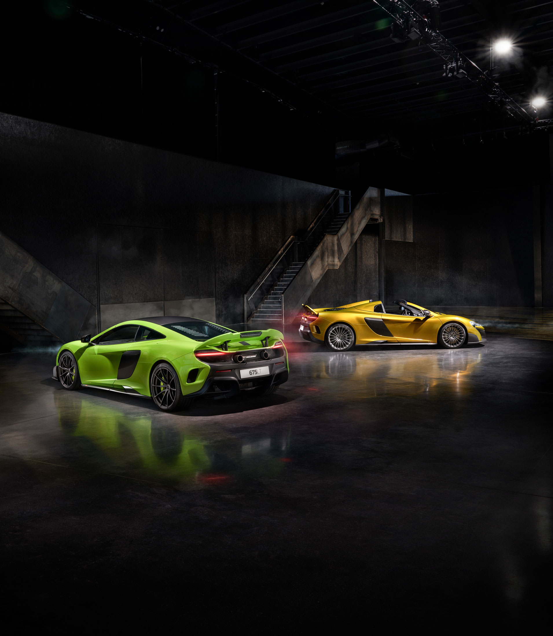 McLaren 675LT Coupe in green and 675LT Spider in gold, parked in a dimly lit industrial setting, showcasing aerodynamics