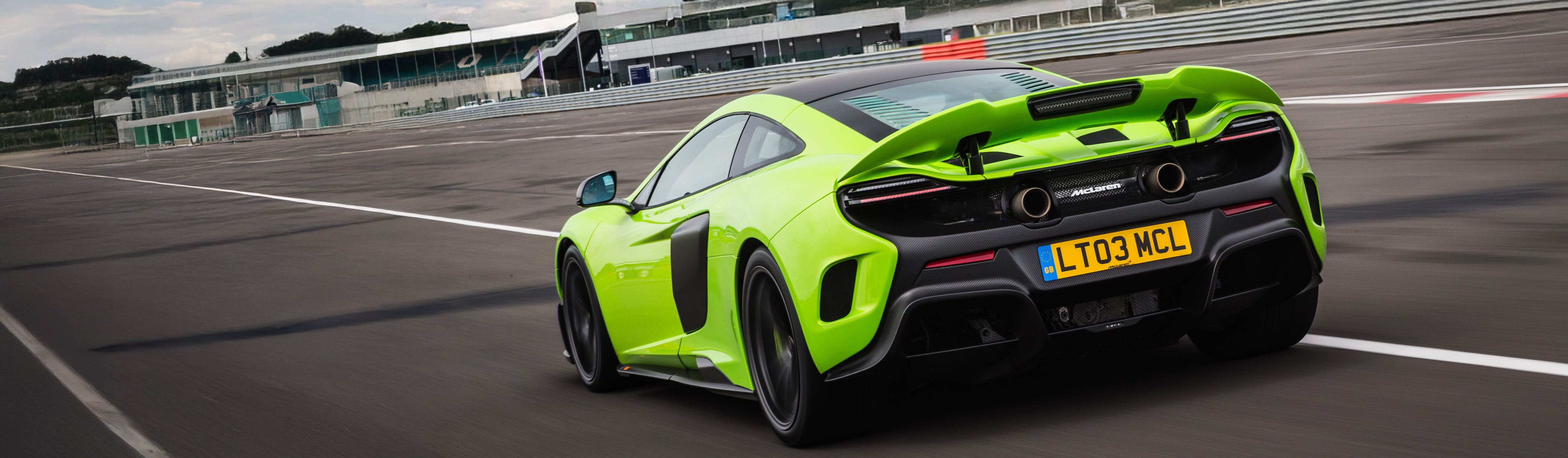 A vibrant green McLaren 600LT is captured from a rear-three-quarter view on a racetrack, showcasing its aggressive rear spoiler, dual top-exit exhausts, and large diffuser.