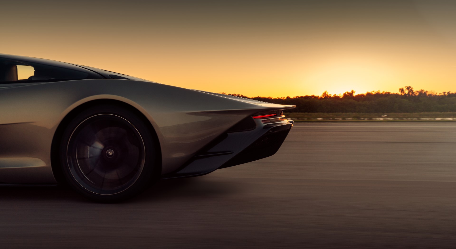 Close up side view of a grey McLaren Speedtail rear as the car drives down a road at speed during sunset.