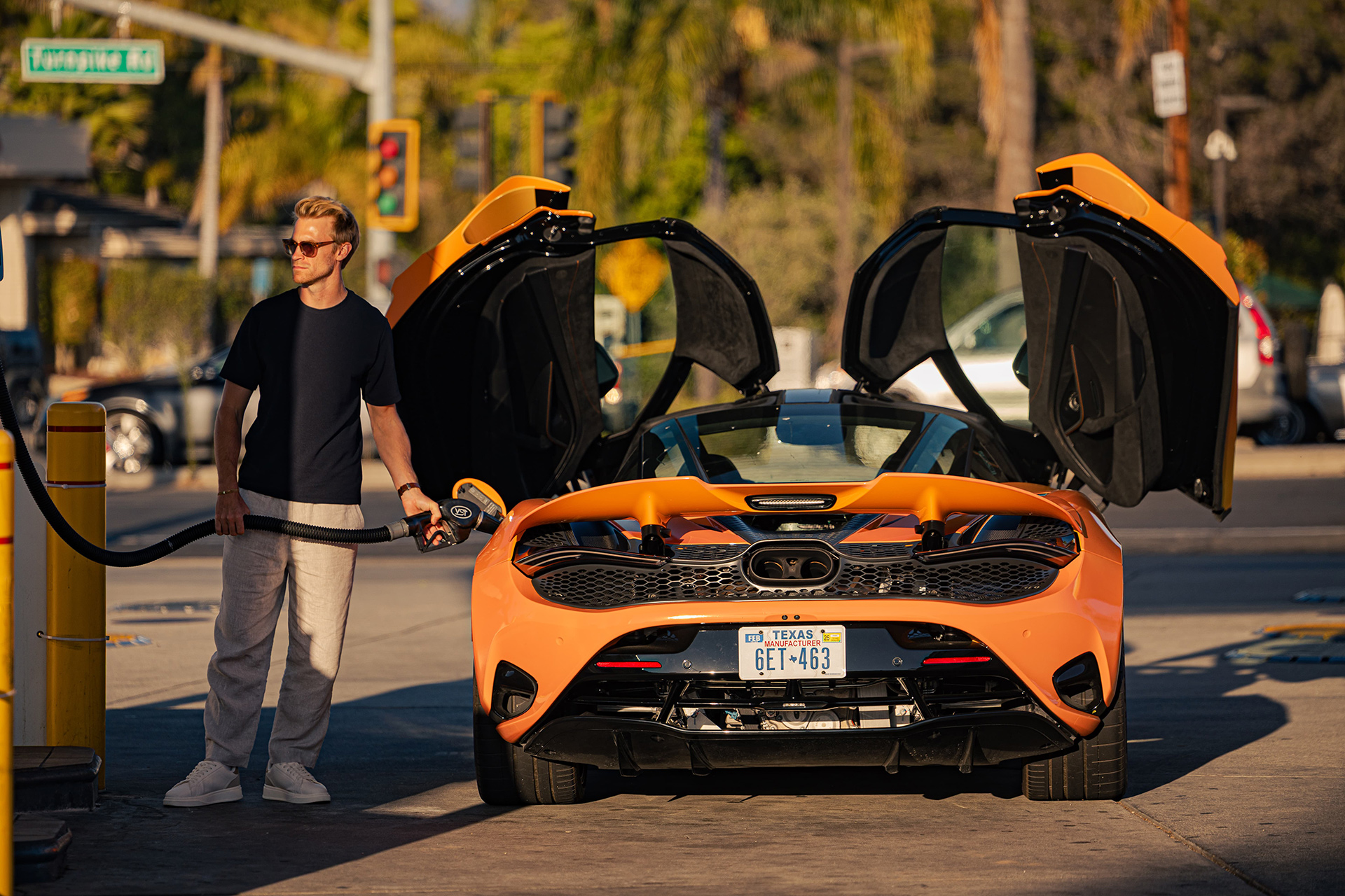 A man is shown filling an orange McLaren 720S with gas, with the car's dihedral doors open, during a stop on the 'States of Endurance' road trip.