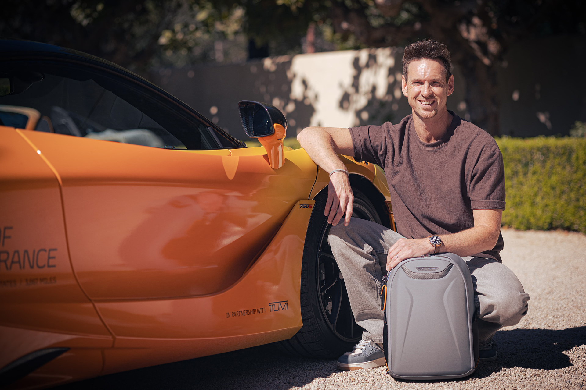 McLaren driver with the TUMI McLaren backpack next to an orange McLaren Artura, highlighting the 'States of Endurance' partnership.
