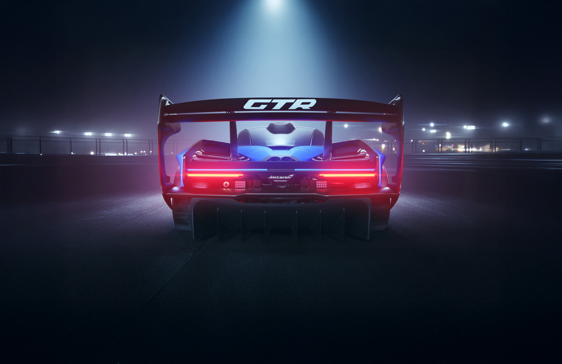 Rear view of a blue patterned McLaren Senna GTR parked in a urban setting at night with brake lights on.