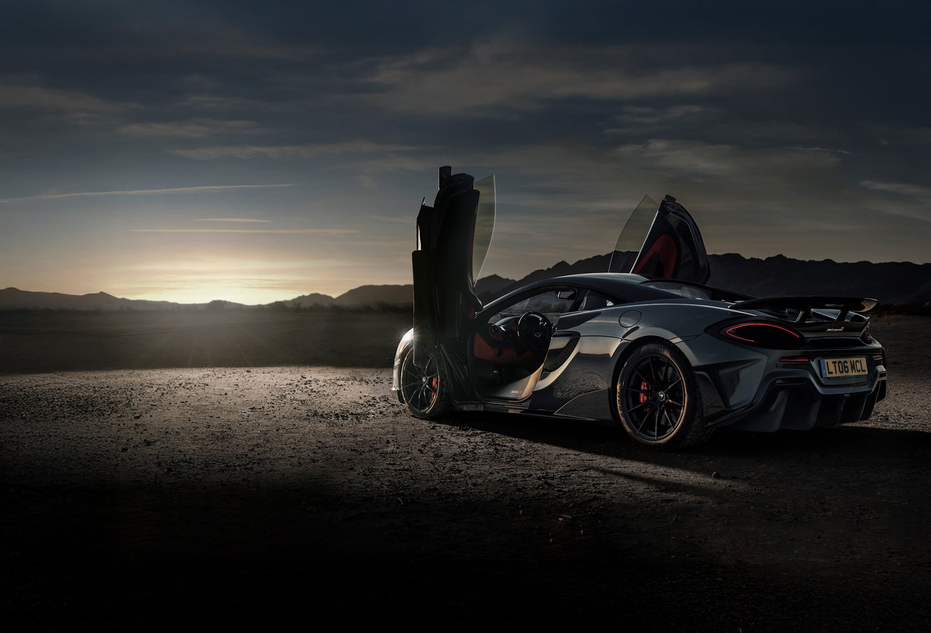 Grey McLaren 600LT parked on a cliff edge with dihedral doors open.