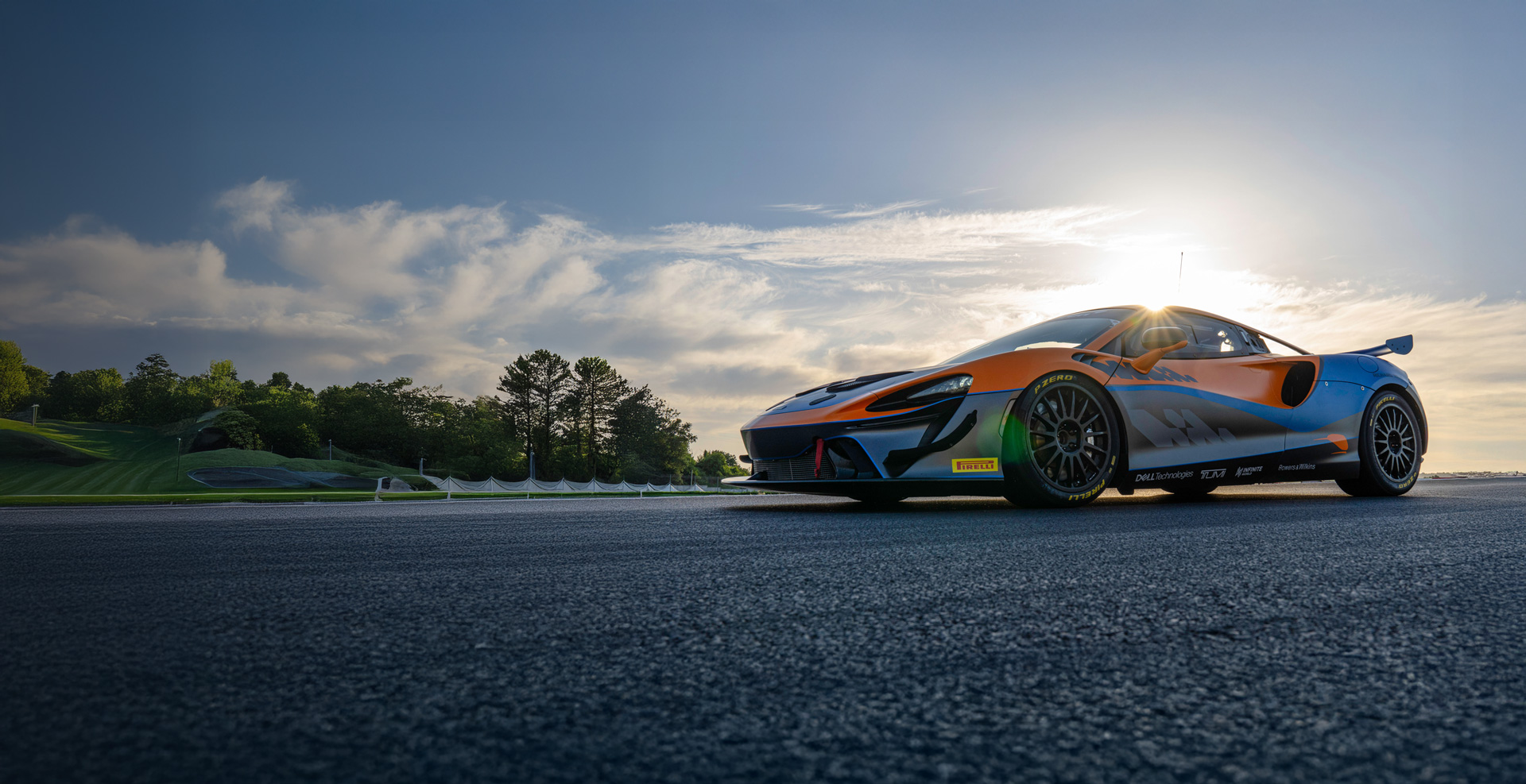 Low shot of a McLaren Artura GT4 parked on a track, with the sun behind it.
