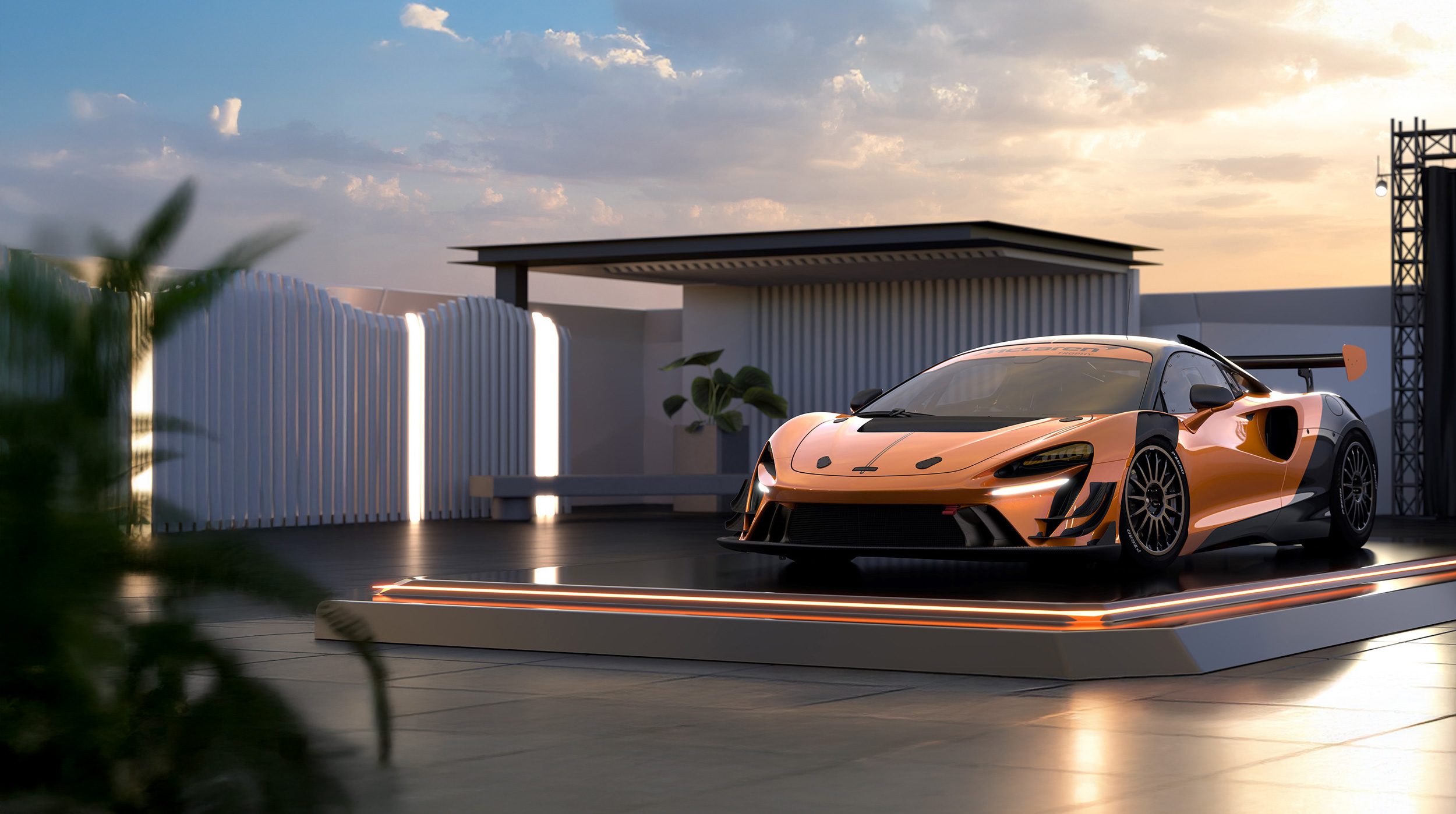 A copper McLaren Artura Trophy EVO parked on a lit up podium, on the rooftop of a modern building, at sunset.