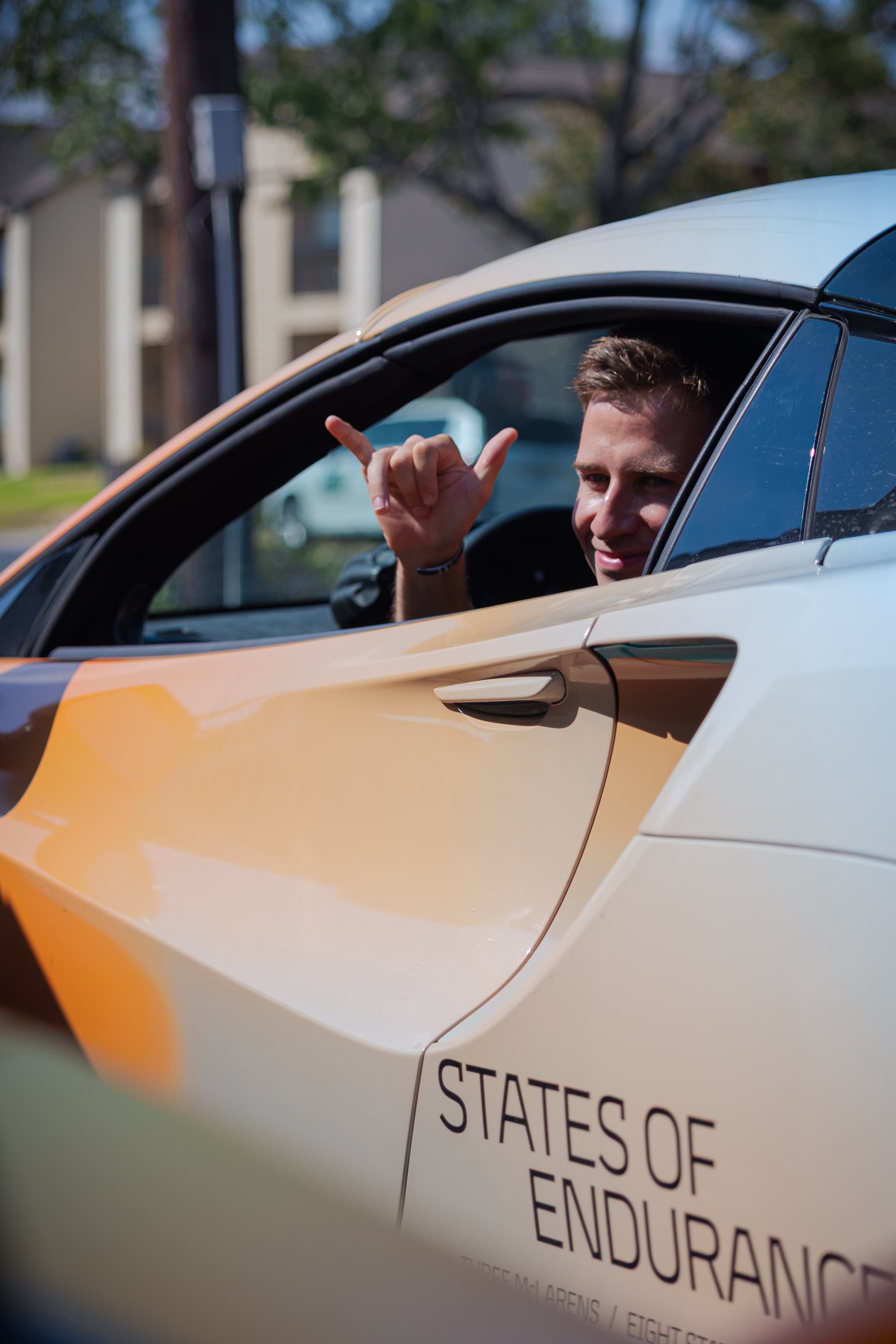 Jack Barlow signing a hang loose hand signal out the drivers side window of his McLaren. A scene from Day 5 of the 'McLaren States of Endurance' road trip.