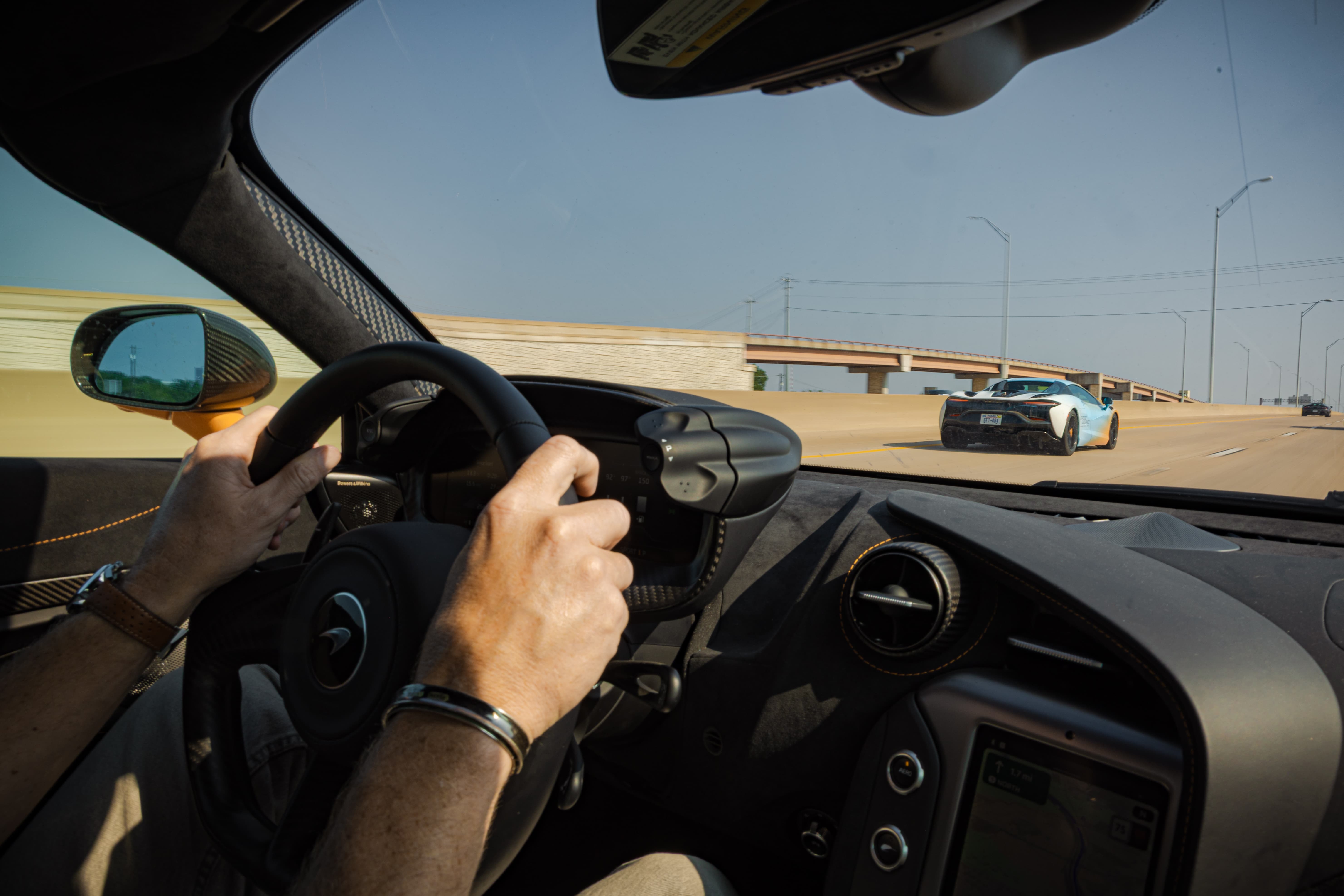 Photo of the interior of a McLaren as it's being driven down a highway. A second McLaren can be seen driving ahead, through the windscreen. A scene from Day 6 of the 'McLaren States of Endurance' road trip.