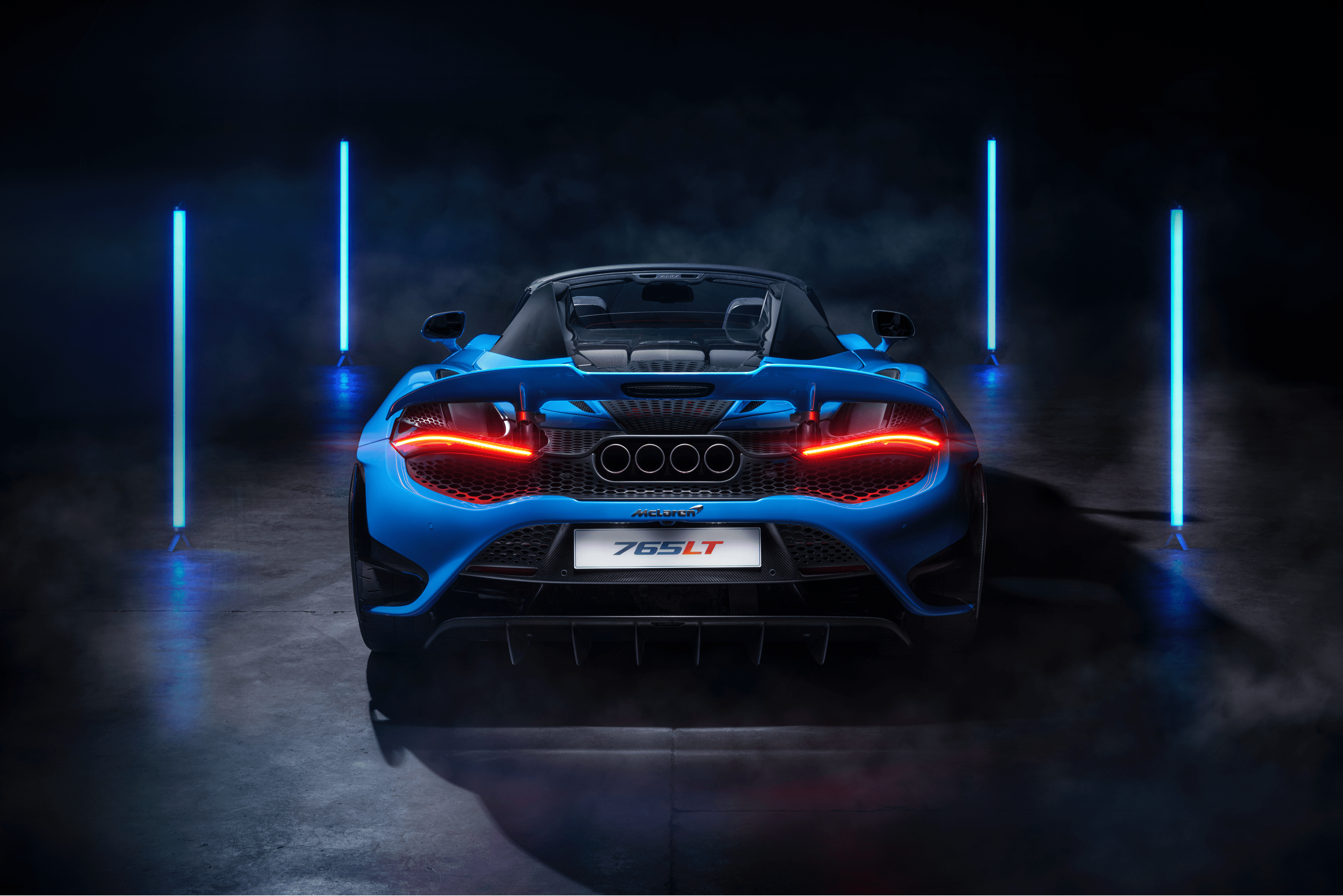 The rear of the McLaren 765LT Spider, with its unique quad exhausts and glowing red taillights, in a dramatic studio setting.