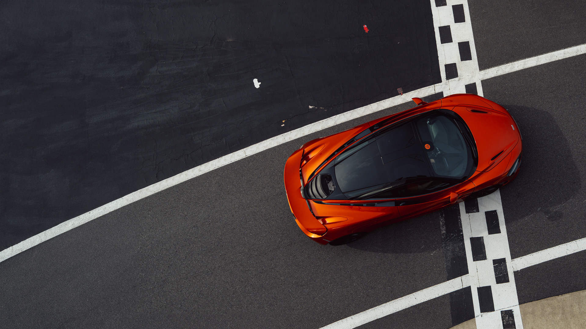 An overhead shot of a burnt orange McLaren supercar stationary on a race track.