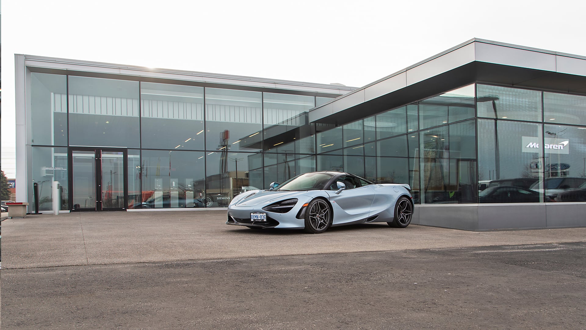 McLaren Toronto (Pfaff) dealership exterior with modern, glass-wall architecture. A silver McLaren 720S Spider convertible is prominently parked out front.