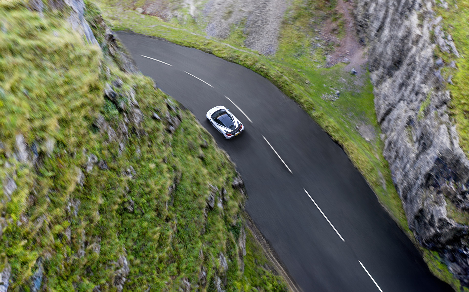 Aerial view of a white McLaren GT driving through Cheddar Gorge.