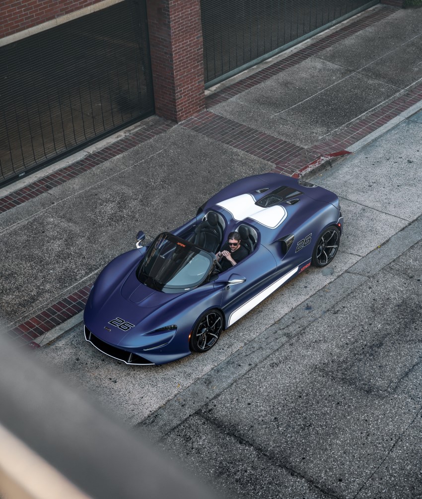 A high-angle shot of a McLaren Elva with a bespoke blue and white livery, parked on a city street with its driver inside.