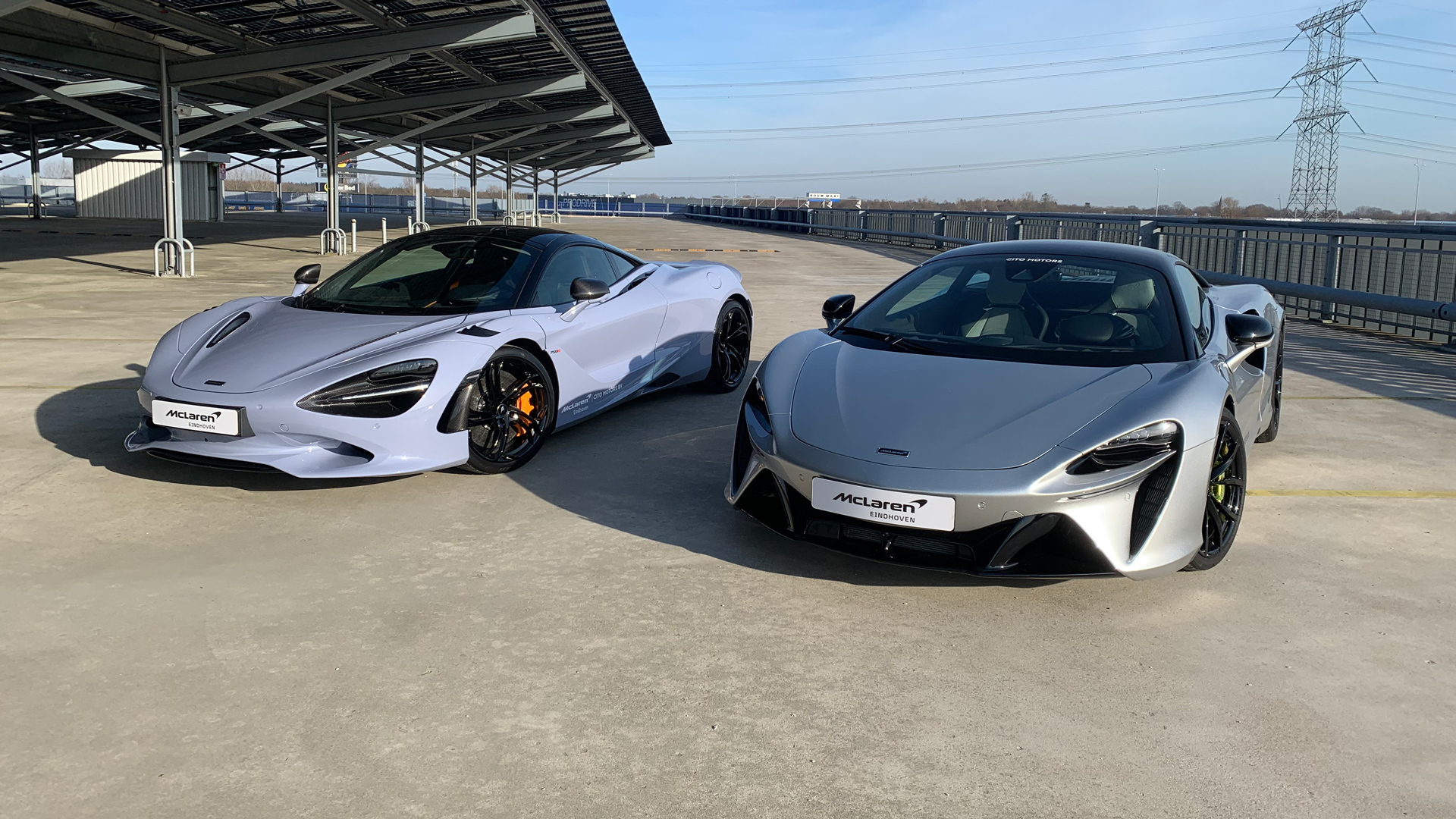 A light grey McLaren 750S and a silver McLaren Artura supercar parked side-by-side in a modern setting, showcasing the latest performance models available at a McLaren dealer.