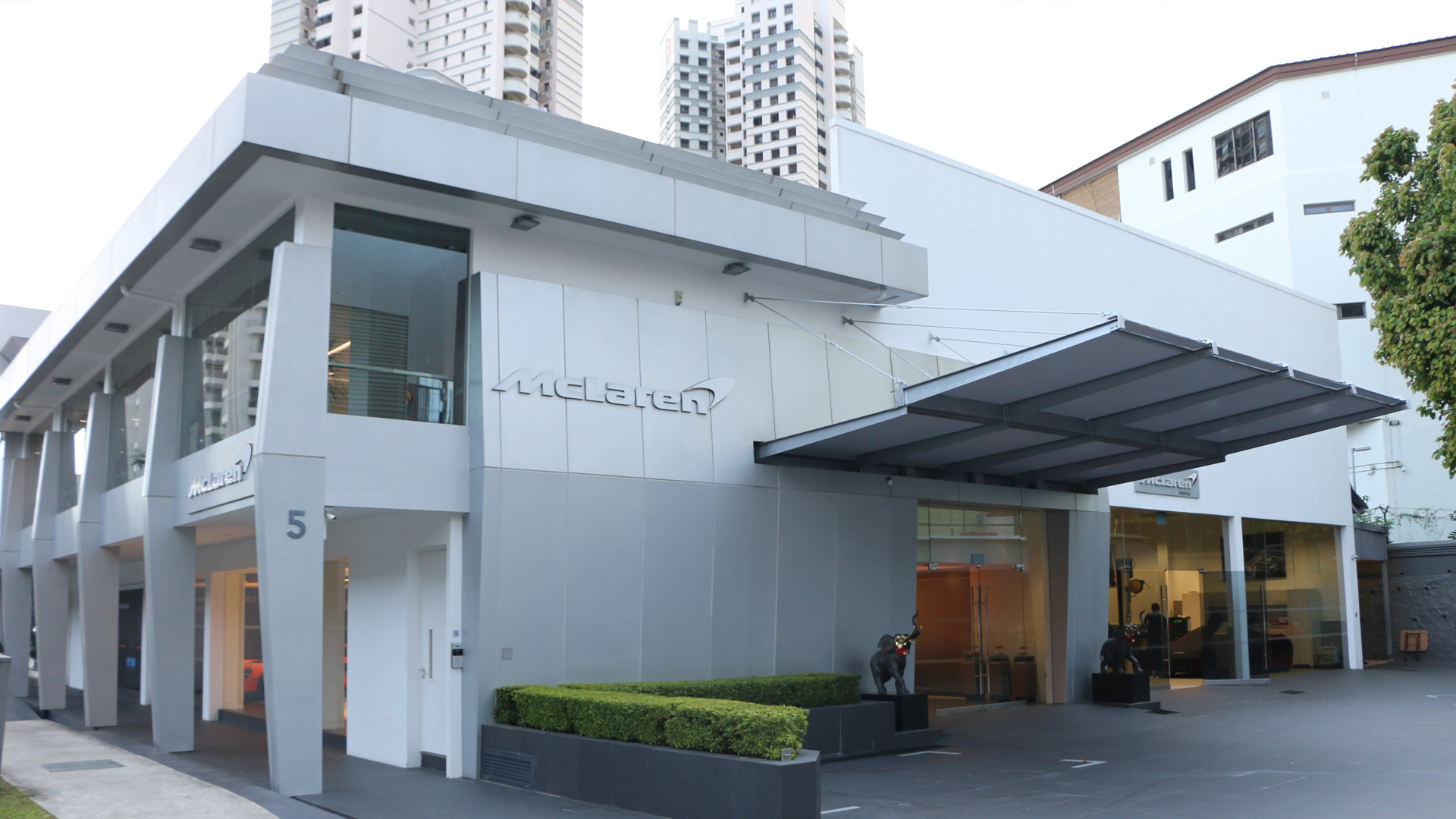 Exterior view of the contemporary McLaren Singapore dealership, featuring a sleek silver facade and glass windows, representing luxury supercar retail in the city-state.