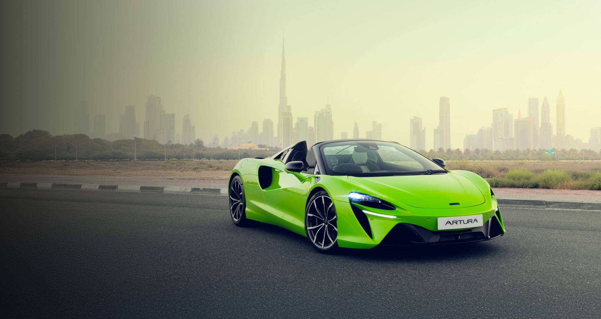 A bright green McLaren Artura parked on a desert road, on the outskirts of Dubai city.
