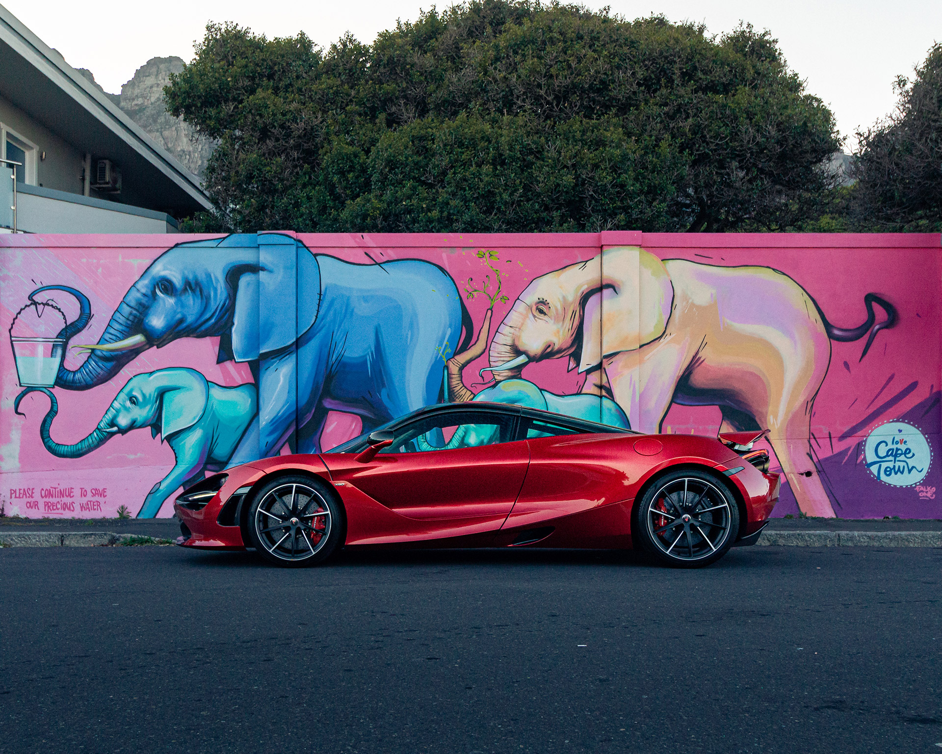 A red McLaren parked in front of a brightly colour mural of elephants in Cape Town