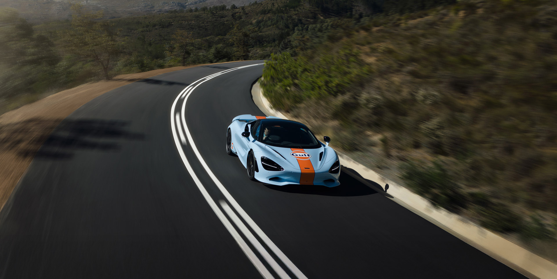 Gulf branded McLaren driving down a rural road. 
