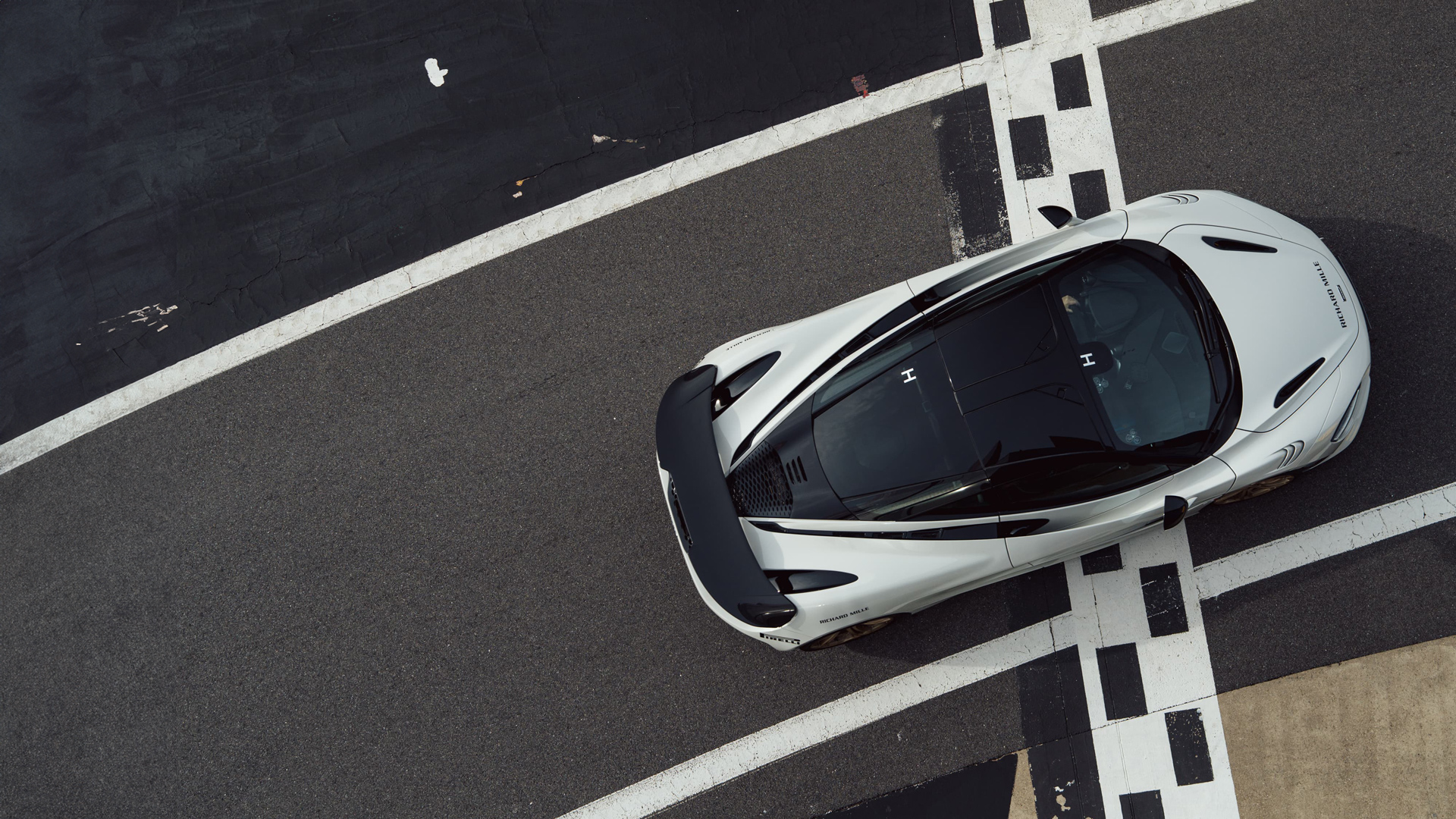 White McLaren Artura high-performance hybrid supercar driving at speed on the Silverstone Grand Prix circuit in the UK, indicated by the track barriers and pit-lane exit area.