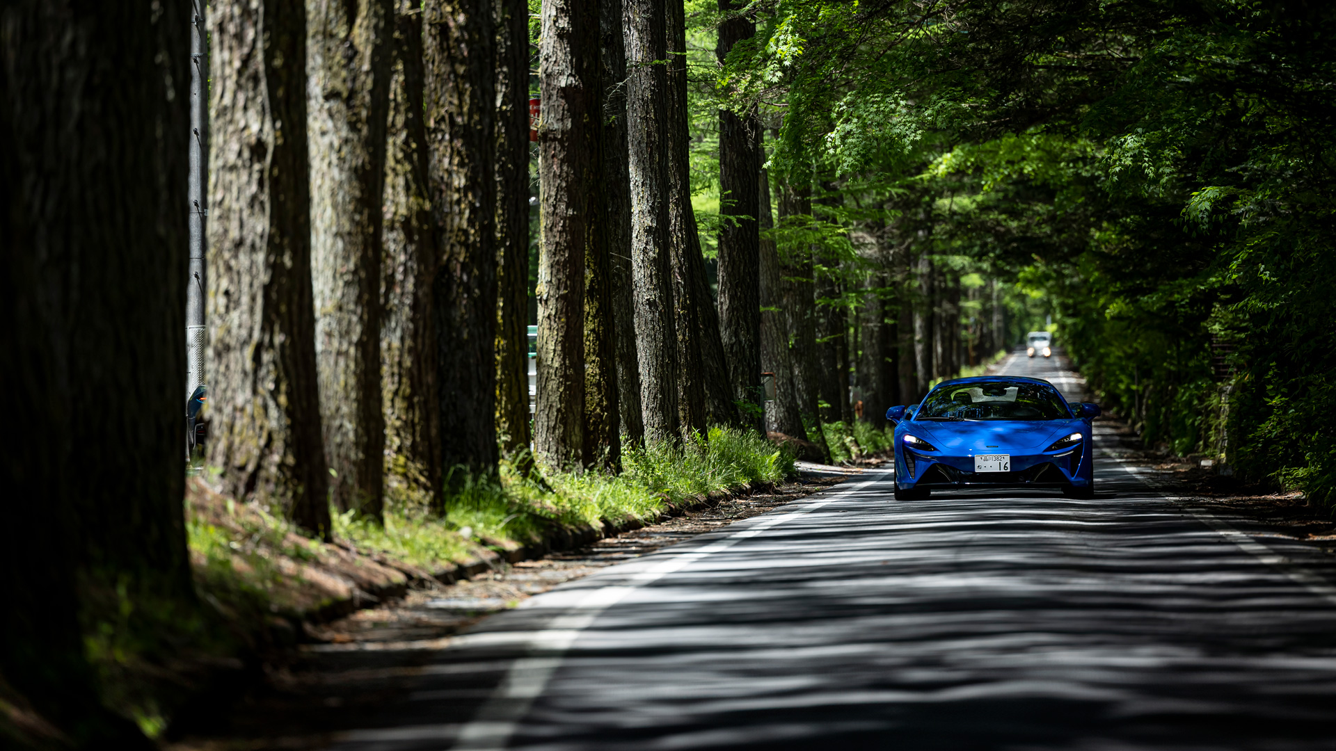 A blue McLaren driving along a road with rows of trees either side.