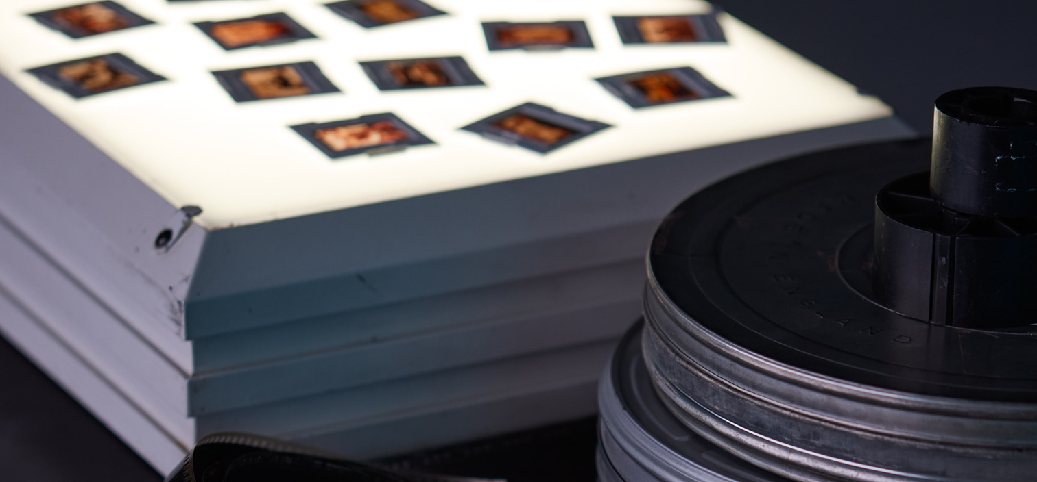 Film slides arranged on an illuminated lightbox beside a stack of metal film reels.