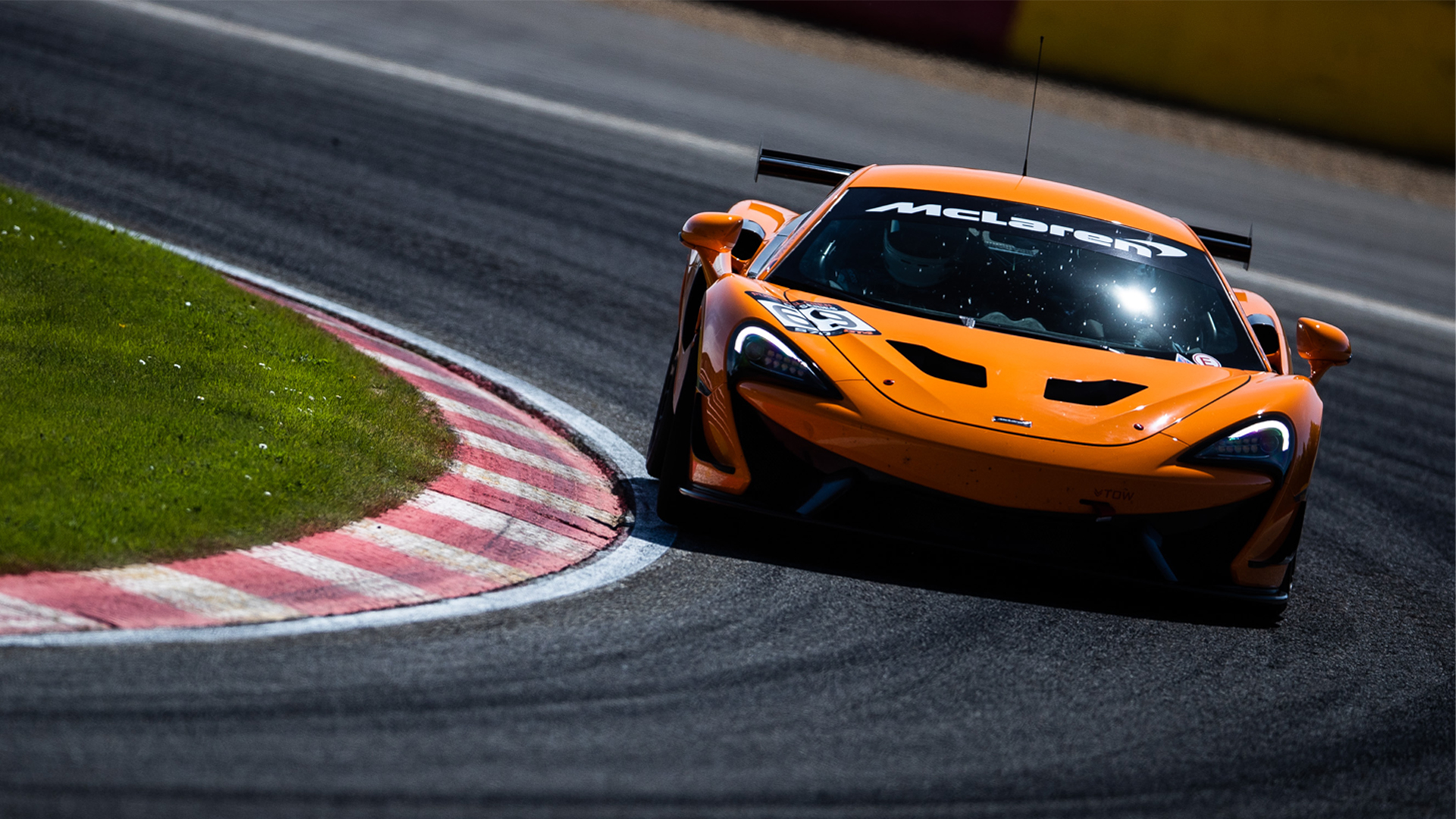 Orange McLaren 570S GT4 driving around a track at speed. 