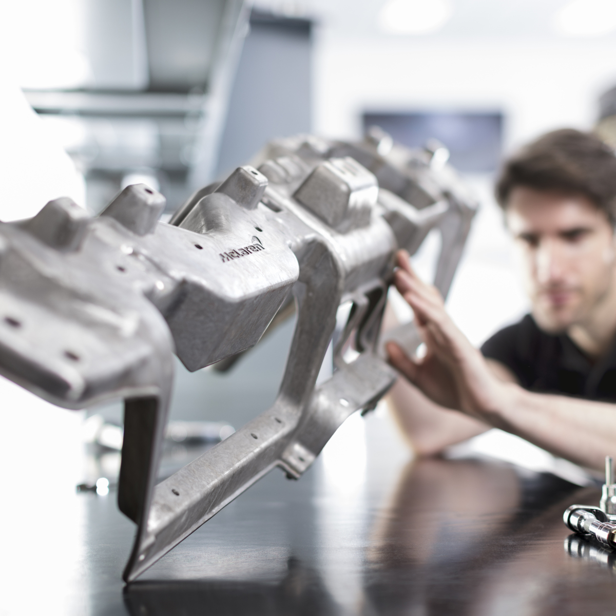 A male McLaren engineer inspecting a car component in a workshop.