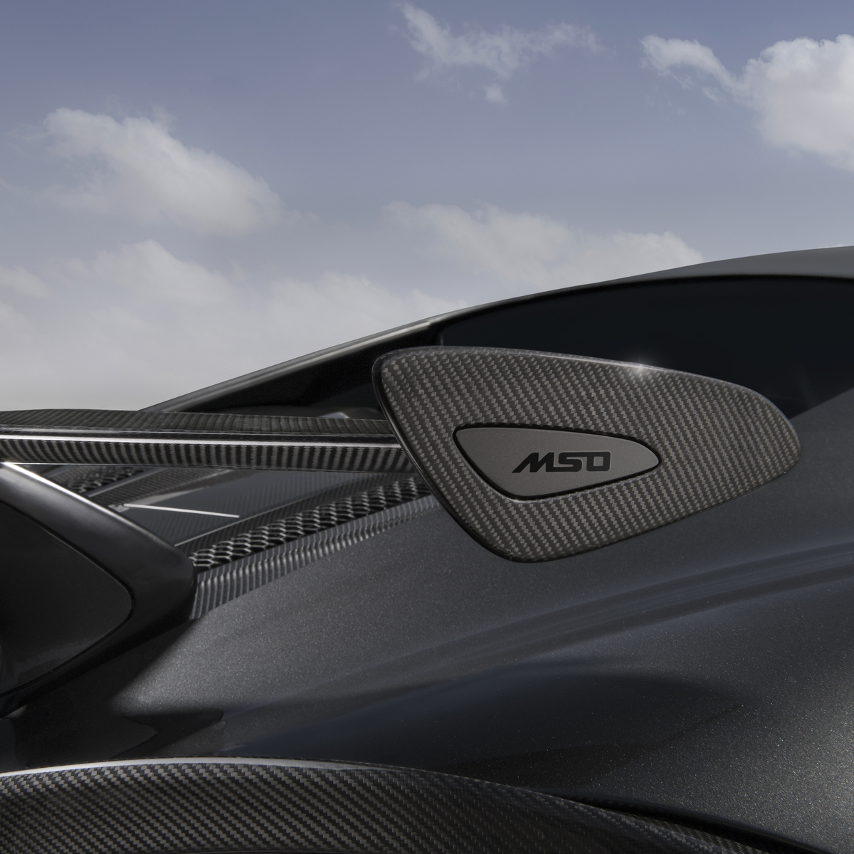 A close-up shot of the carbon fiber side mirror on a grey McLaren 600LT. The 'MSO' logo is visible on the mirror housing, highlighting the McLaren Special Operations customisation.